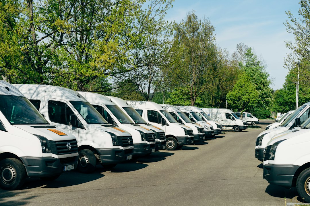 Vans brancas estacionadas lado a lado em um pátio arborizado